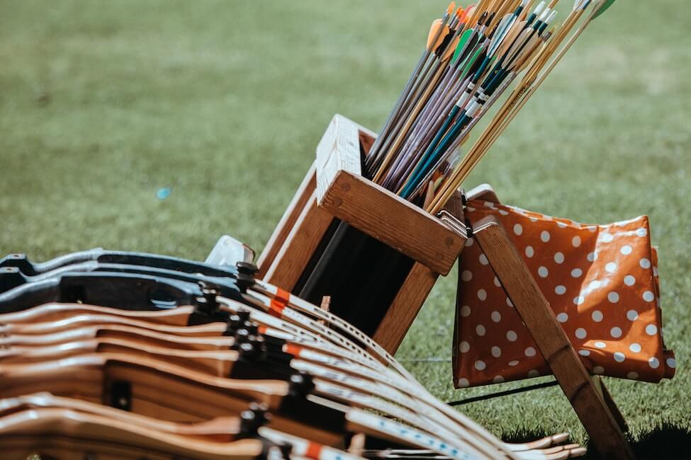 Lots of wooden bows stacked up with a container of arrows.